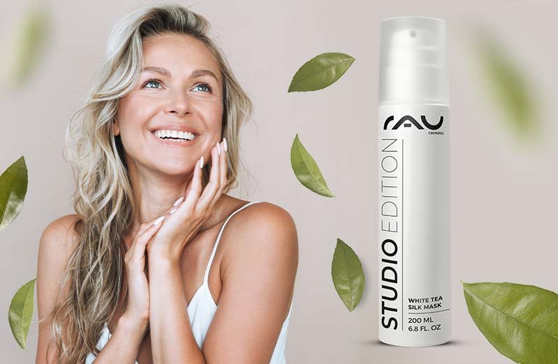 Lächelnde Frau mit langem, gewelltem Haar und "STUDIO EDITION" White Tea Skin Mask von RAU Cosmetics in der Hand.