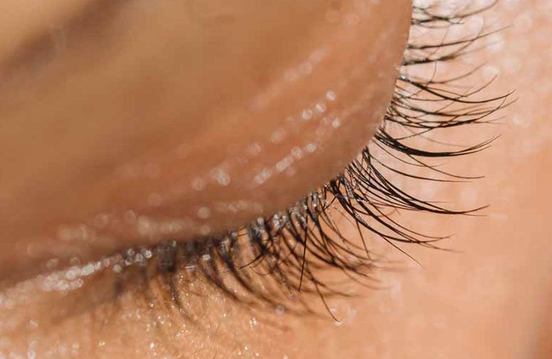 Nahaufnahme eines geschlossenen Auges mit langen, geschwungenen Wimpern, betont die empfindliche Augenpartie und die Bedeutung von spezieller Augenpflege.