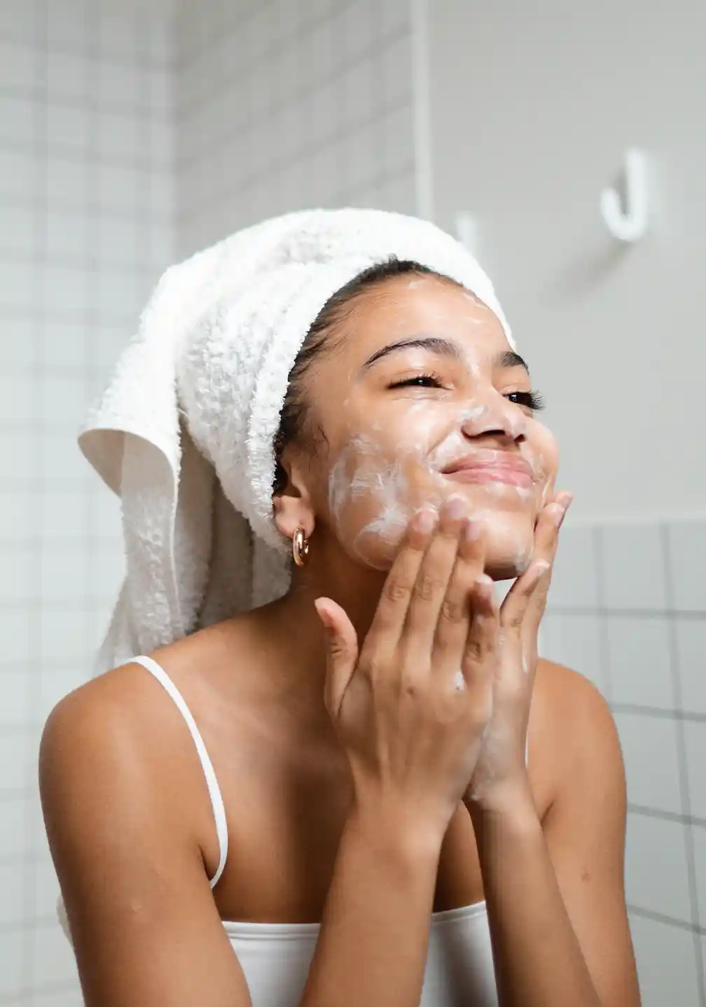 Junge Frau wäscht ihr Gesicht im hellen Badezimmer mit RAU Cosmetics Beta Glucan Recovery Mask und frischem Handtuch.