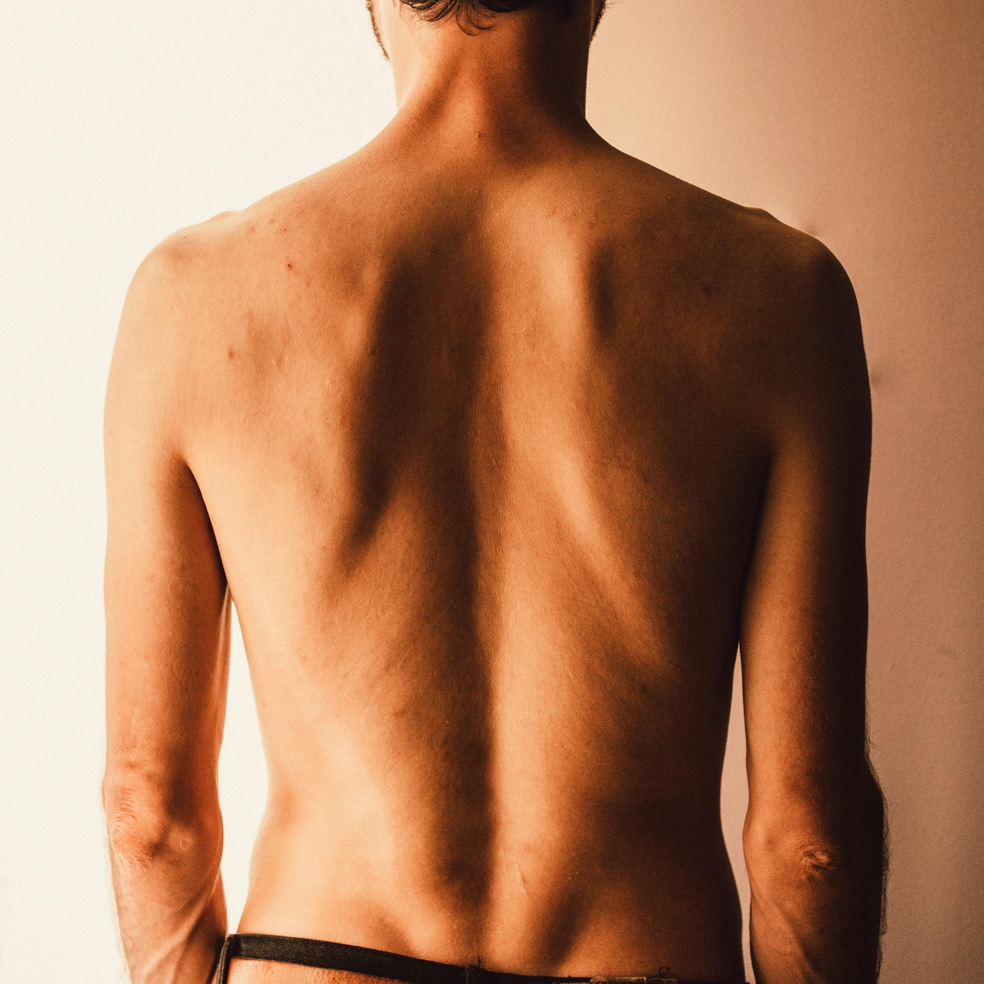 pexels-juanpphotoandvideo-1081672 Frau mit Rückenansicht, die sich mit beiden Händen über die Schultern streckt, während sie in einem weißen Badetuch vor einem Spiegel steht.