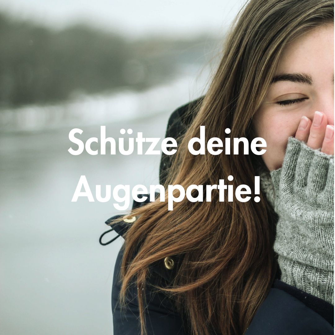 Schtze deine Augenpartie! Frau mit geschlossenen Augen und Händen im Gesicht, trägt graue Handschuhe, Text "Schütze deine Augenpartie!", winterliche Umgebung, thematisiert Augenpflege im Winter.