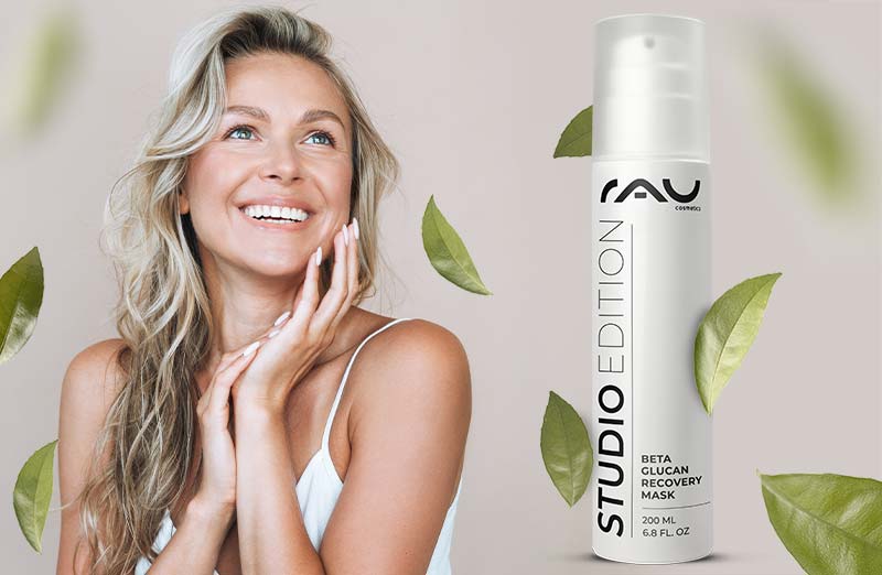Frau mit fröhlichem Gesicht verwendet Beta Glucan Recovery Mask von RAU Cosmetics, umgeben von grünen Blättern.